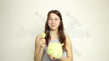 美丽的年轻女人吃蔬菜。 抱着卷心菜，她盯着卷心菜的头。 健康食品-健康食品